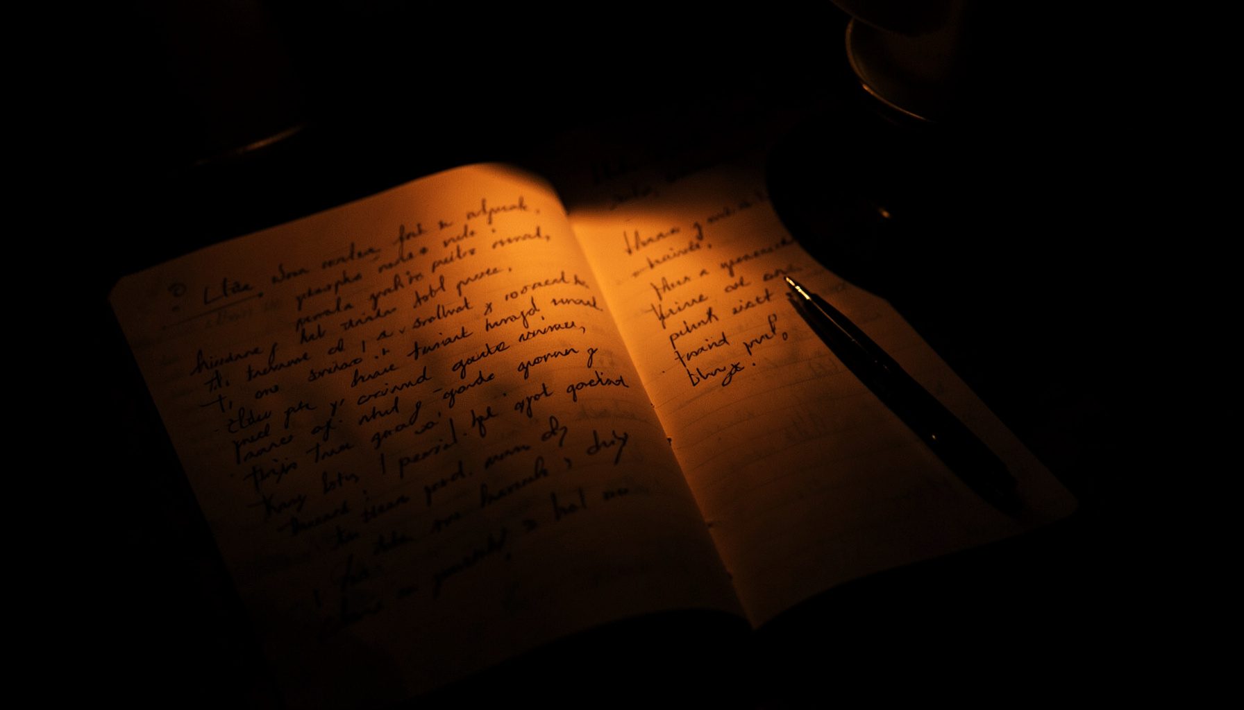 Dark, low-key photograph of an open journal with handwritten reflections, a pen resting beside it, warm lamplight.